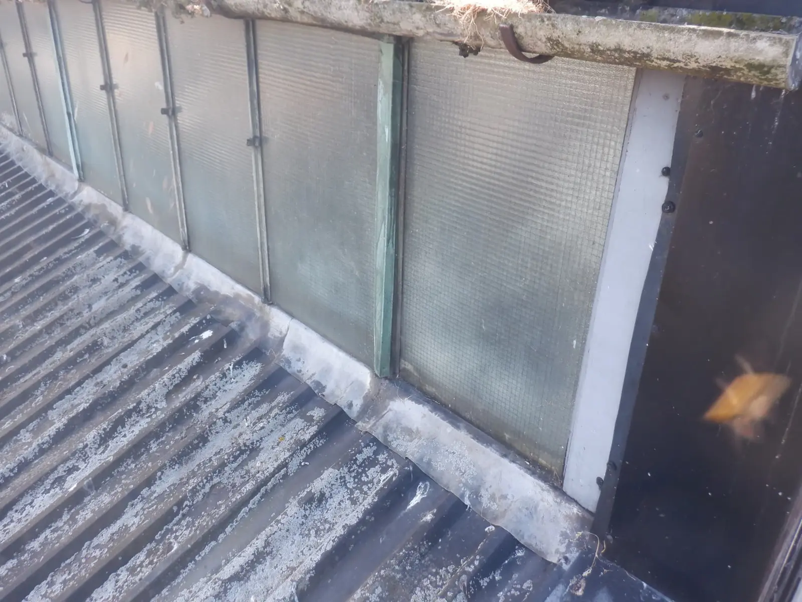 Existing metal roof upstand and rooflight interface showing limited available height for overcladding