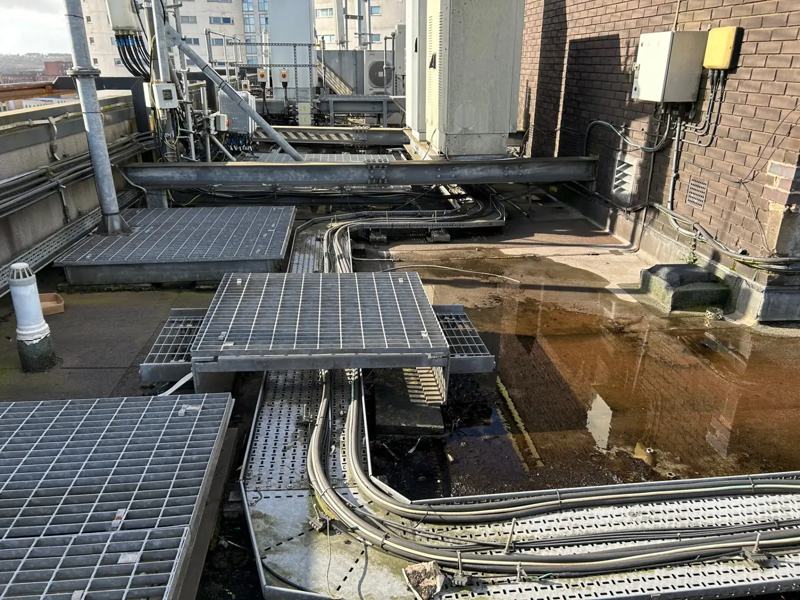 Hospital roof plant area with significant ponding water highlighting water-ingress and equipment risks