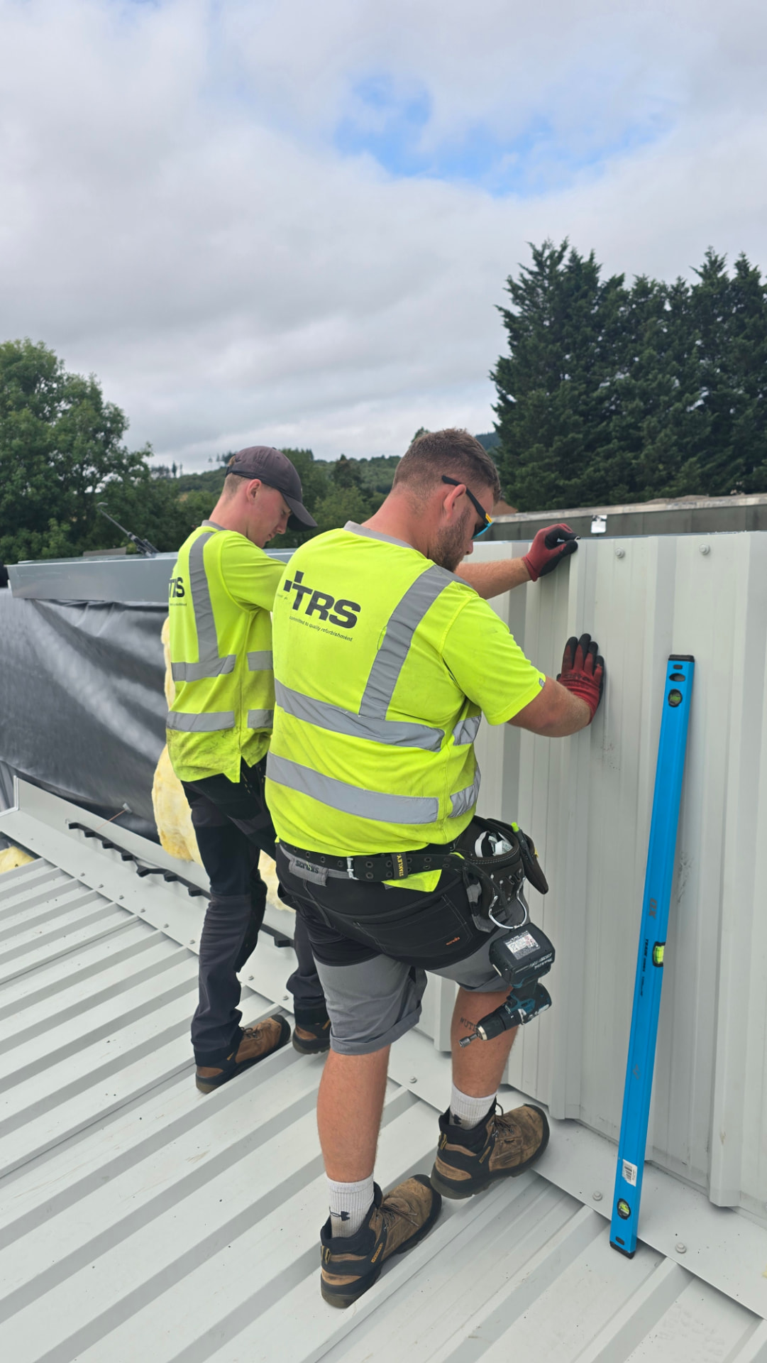 Two TRS roofing operatives fixing flashing detail on a metal roof