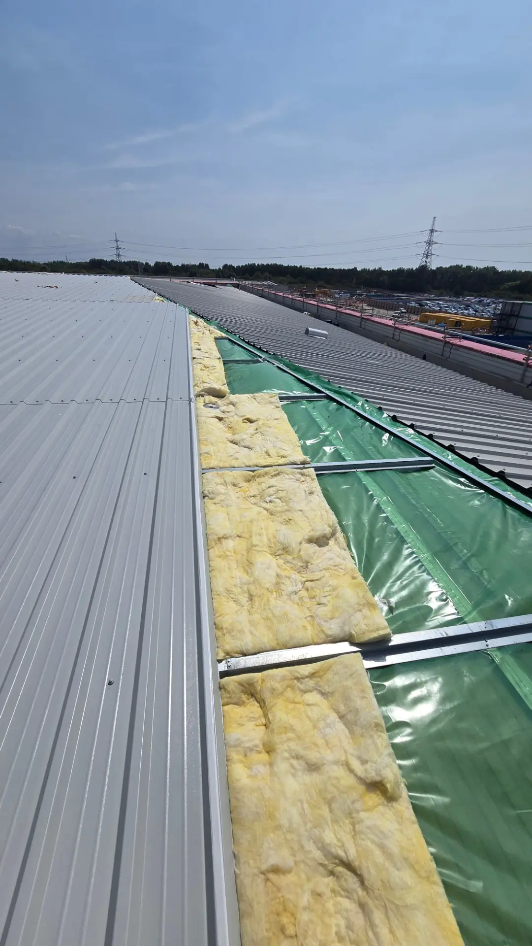 New metal outer sheets and insulation being installed over an existing industrial roof during overcladding works