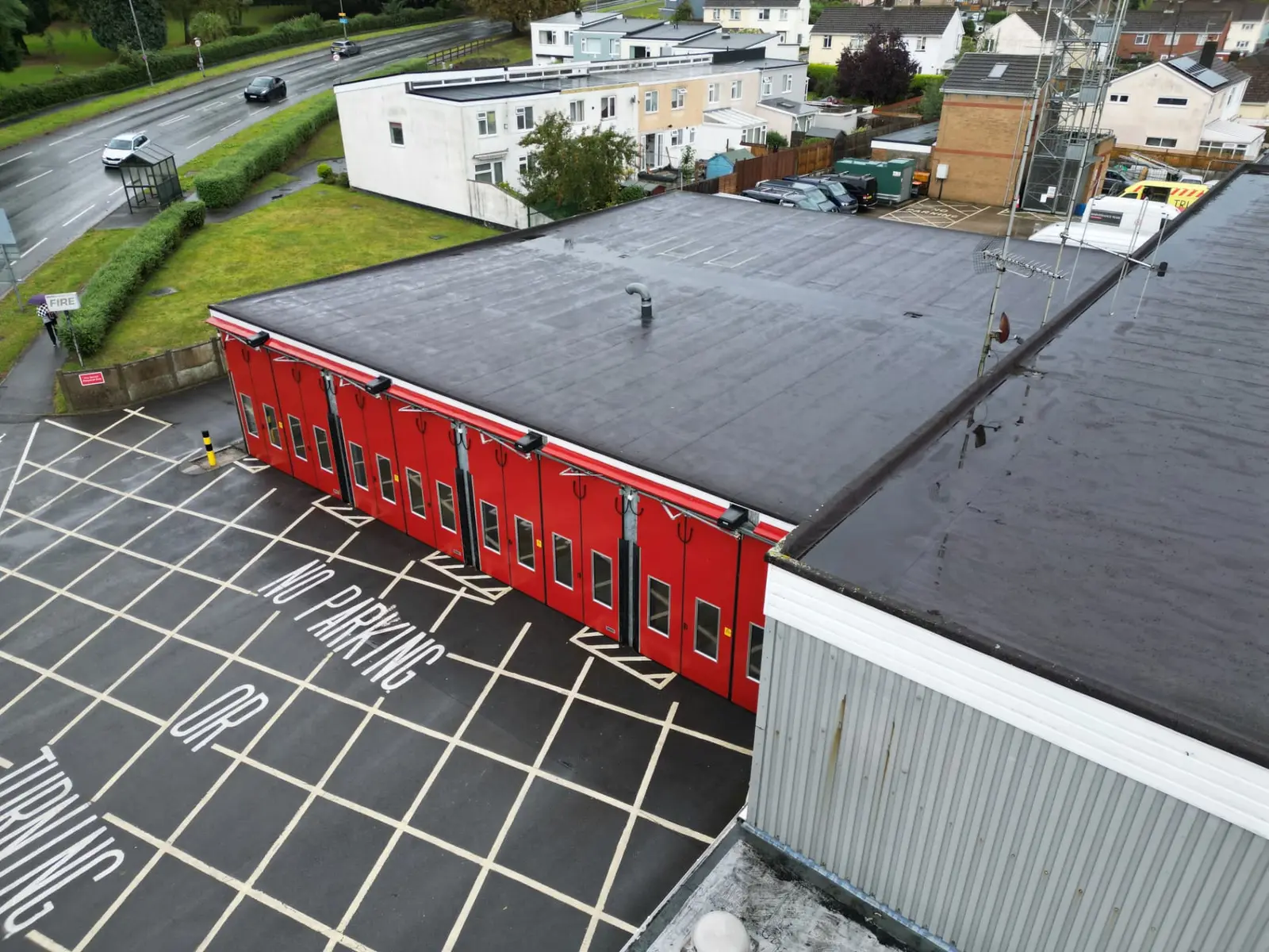 Aerial view of a fire station with a flat roof and red appliance bay doors, an example of an occupied public-sector building