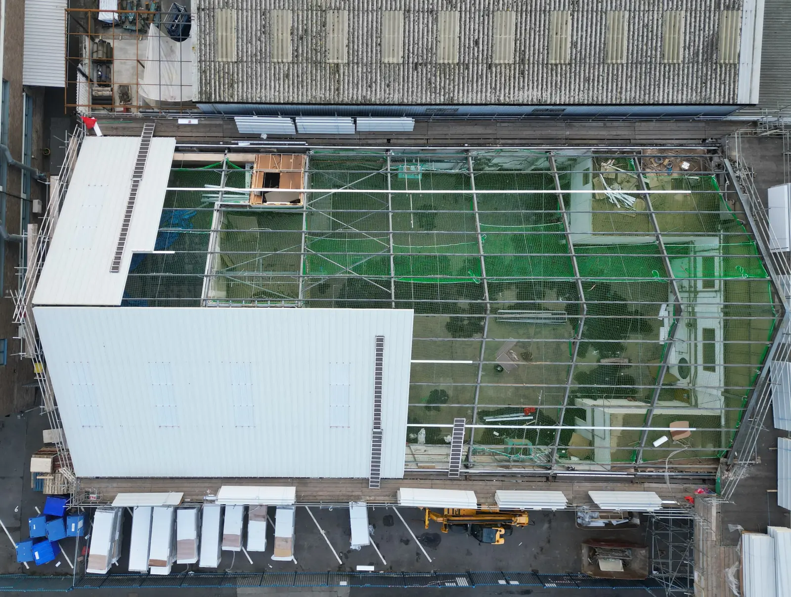Aerial view of industrial roof refurbishment works showing partial new covering, scaffolding and site protection