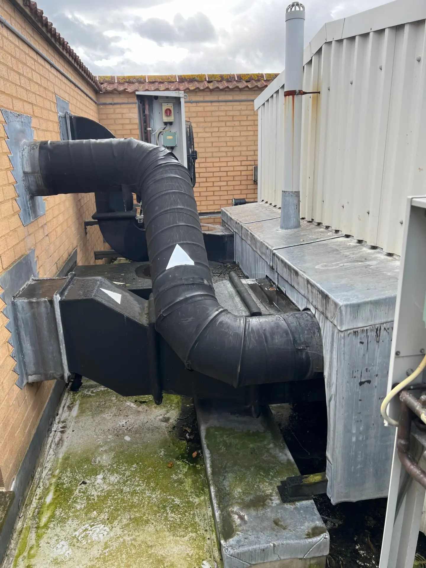 Roof-mounted ventilation plant and ductwork with standing water and algae growth on a hospital roof